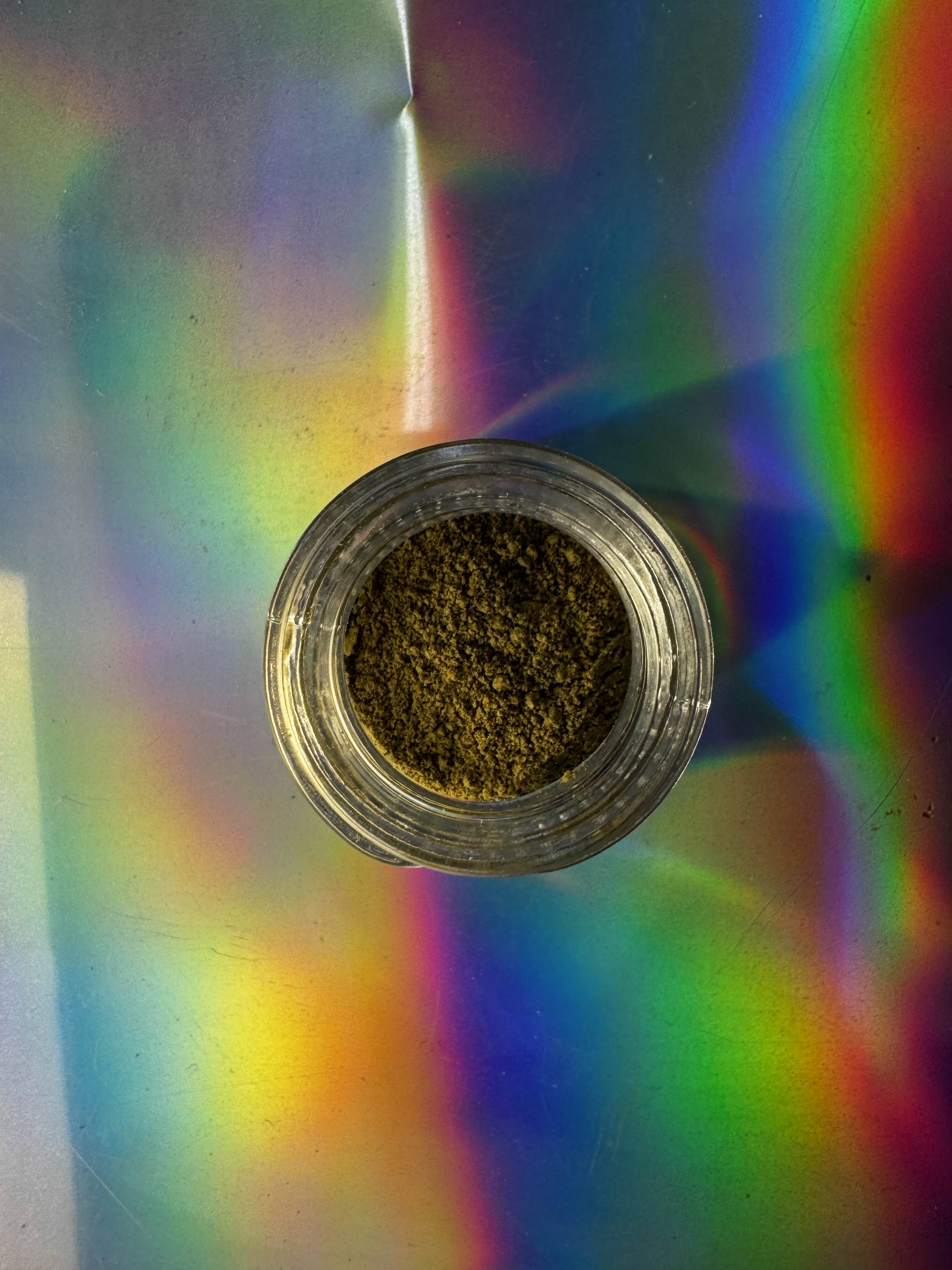 Glass container with brown kanna extract powder product on a colorful, reflective surface.