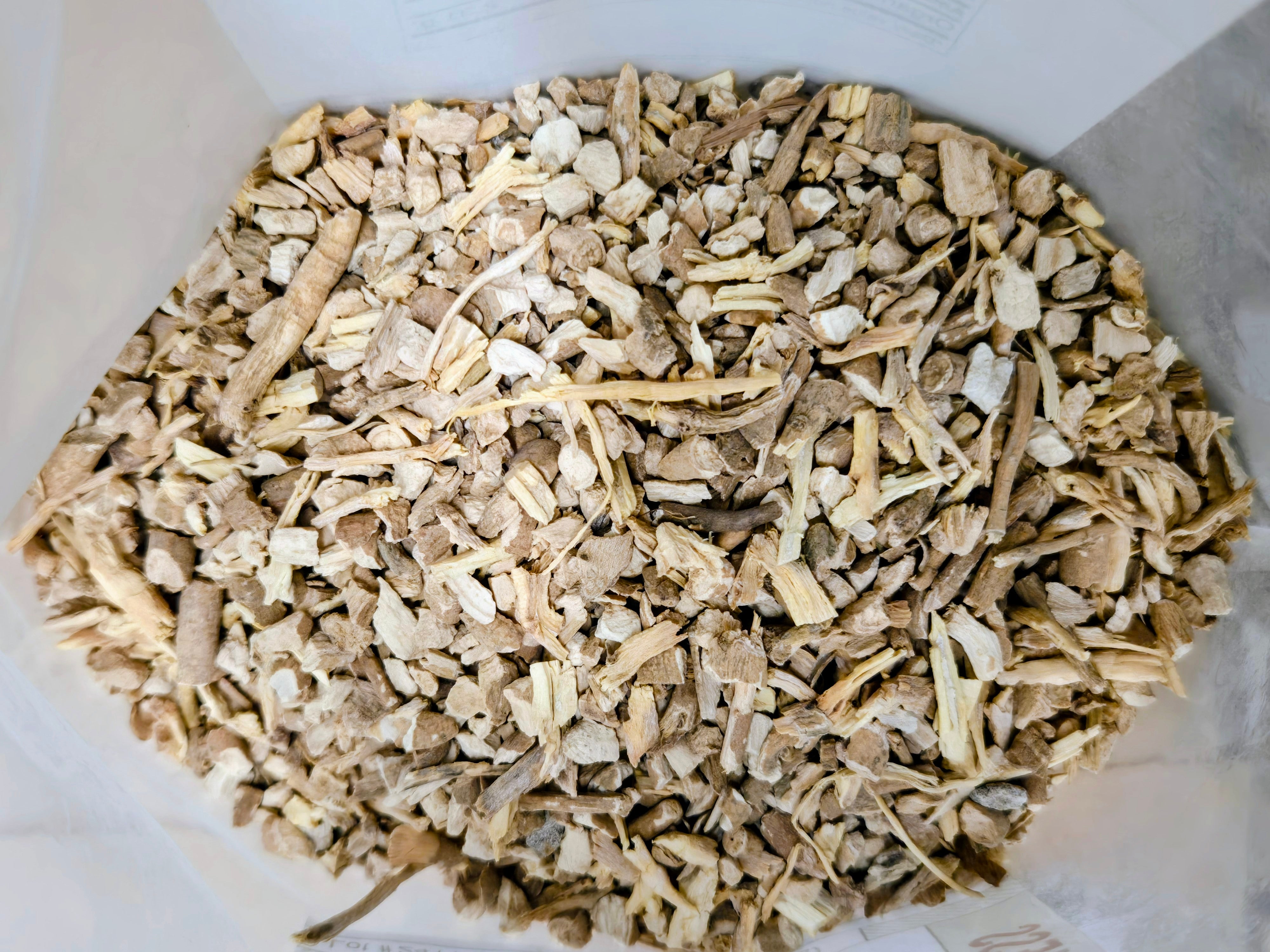 Close-up view of chopped whole ashwagandha root pieces in natural tan and beige tones, showing a coarse, fibrous texture inside an open container.