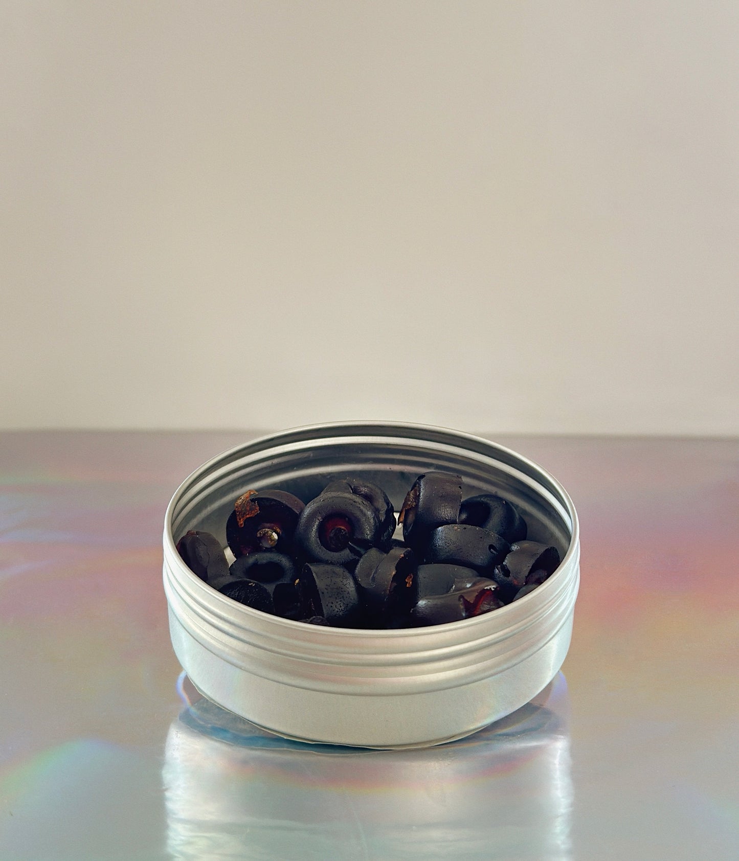 Silver tin with blue lotus gummies in it over a grey slight iridescent background. The gummies are essentially dark black / red. Blue Lotus Gummies