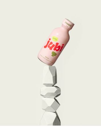 Pink Jubi Kava Chill herbal supplement shot bottle balanced on stacked white geometric stones, strawberry flavored, against a clean light background.