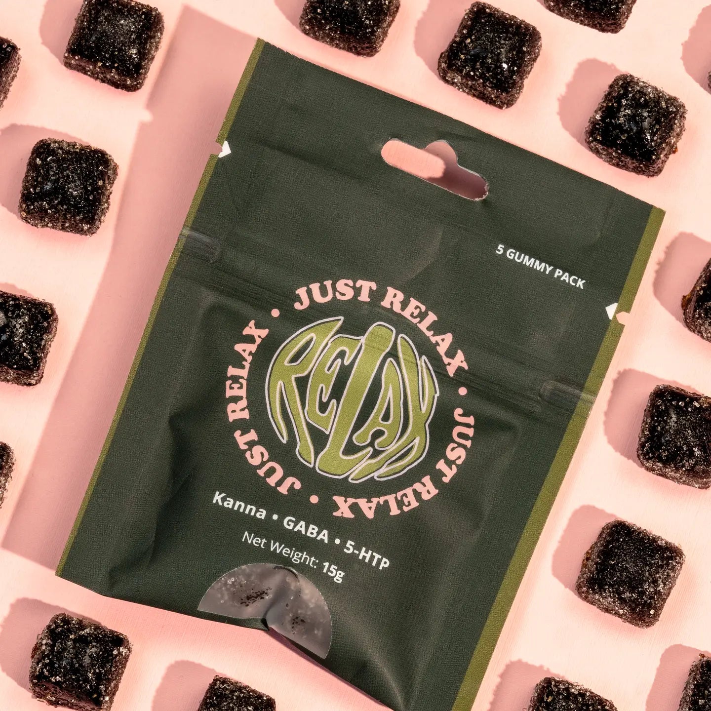 Just Relax functional gummy chews by Healing Herbals in a dark green resealable pouch labeled “Kanna • GABA • 5-HTP,” 5-gummy pack (15g), photographed top-down on a soft pink background with dark cube gummies arranged around the package.