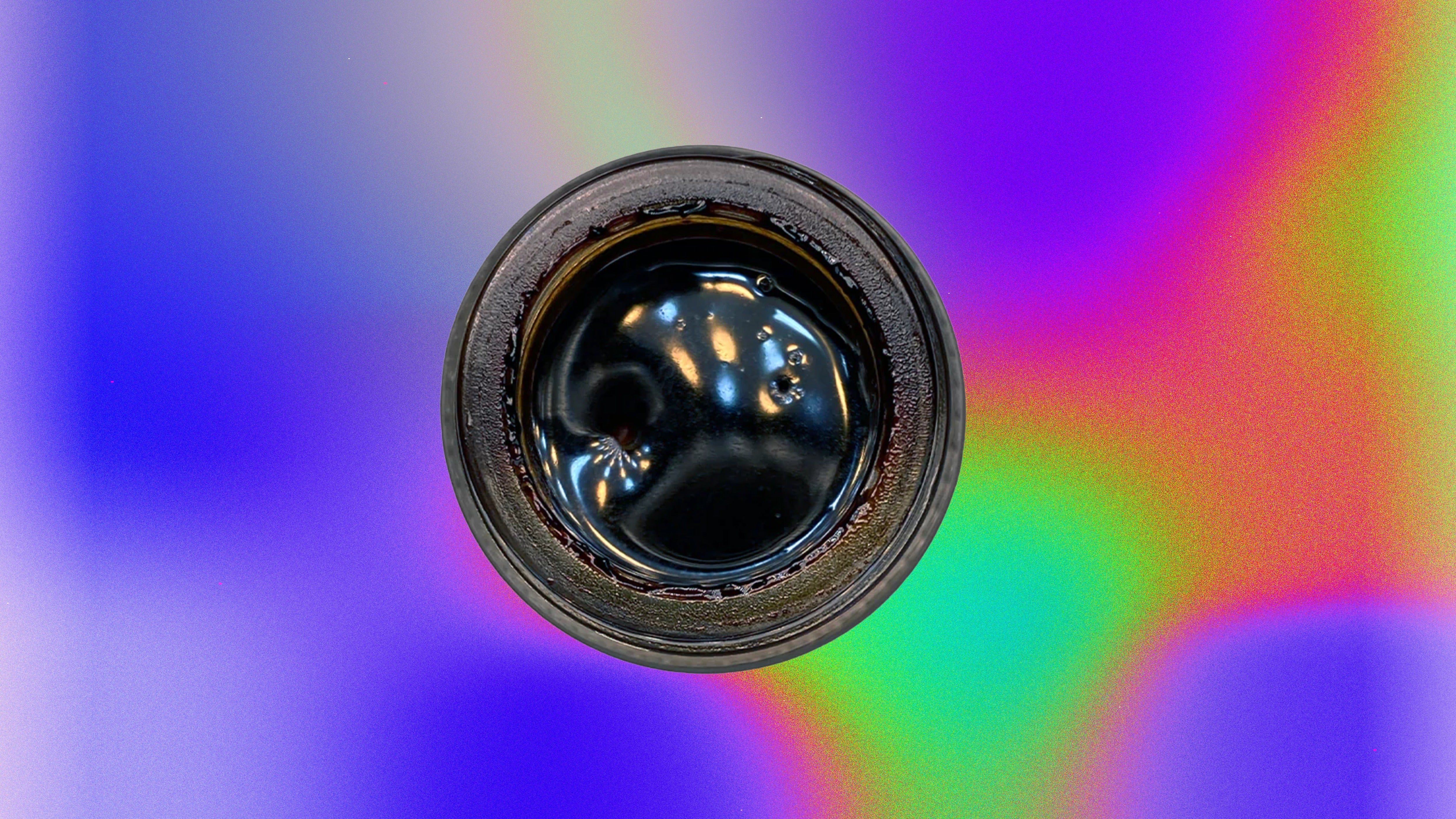 Glass jar filled with dark, shiny resin concentrate photographed from above on a colorful gradient background.
