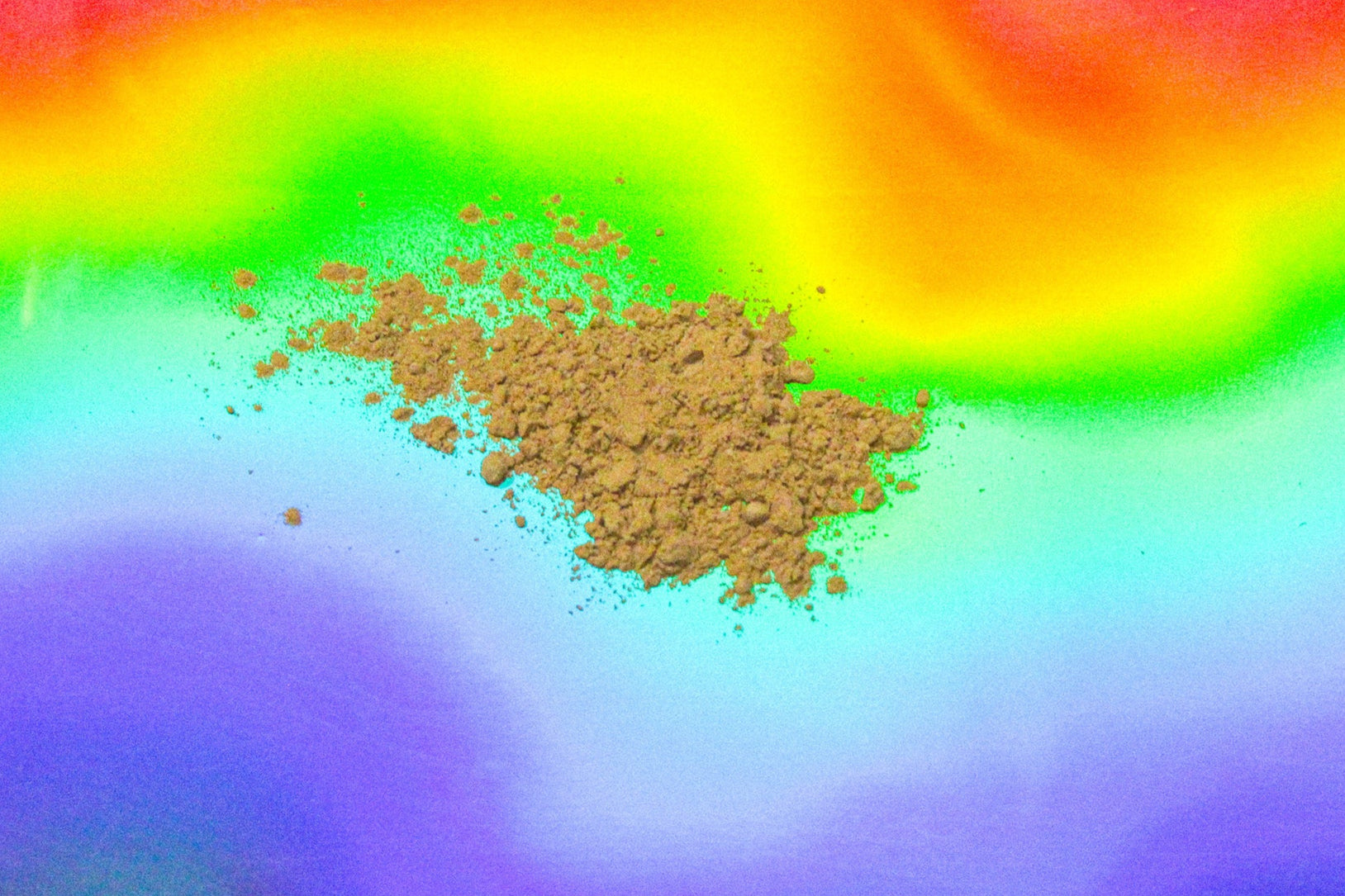 Close-up of micronized kava root powder with a fine light-brown texture, scattered on a vibrant rainbow gradient background.
