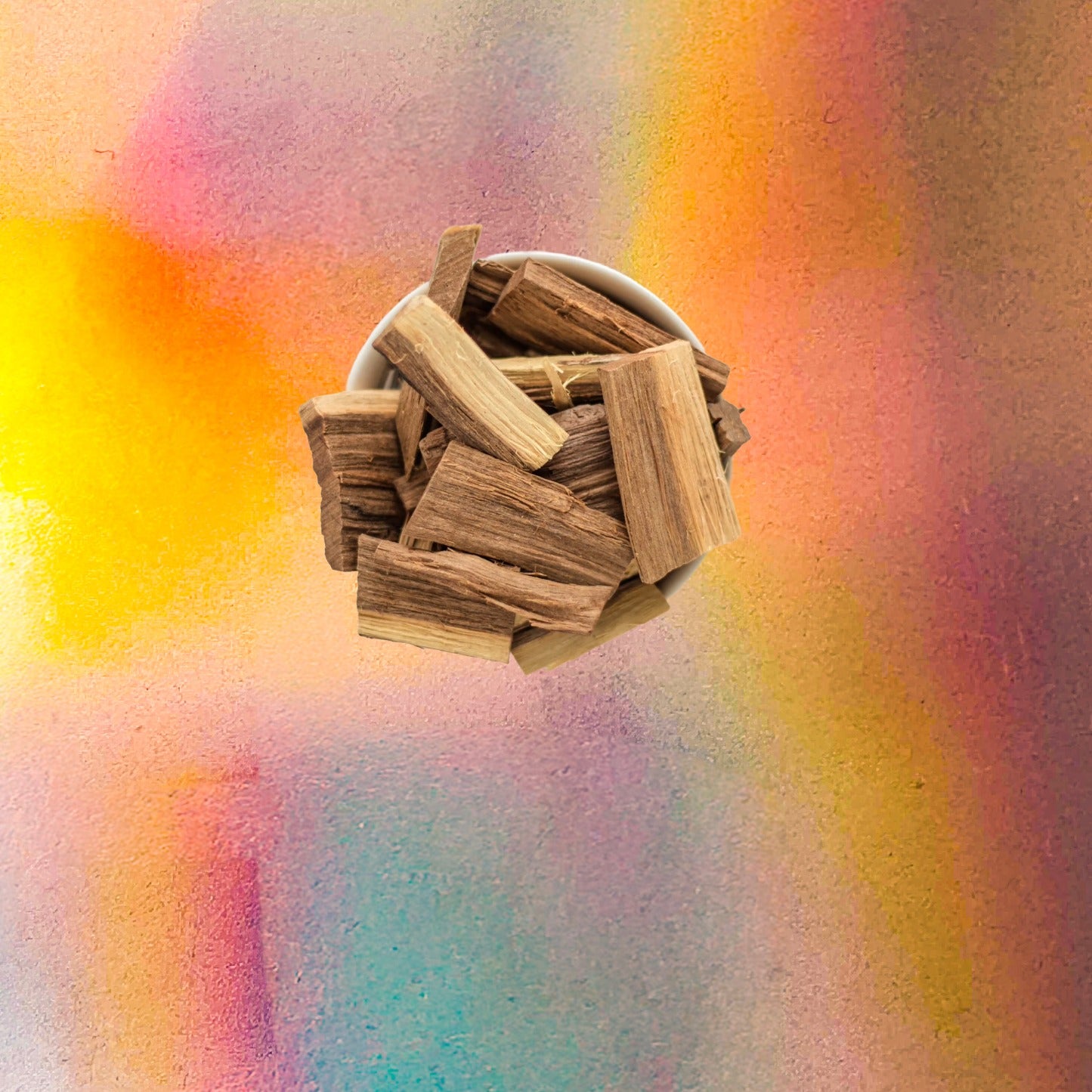 Top-down view of a small white bowl filled with short natural wood sticks, placed on a vibrant iridescent background with warm yellow, pink, and blue color reflections.