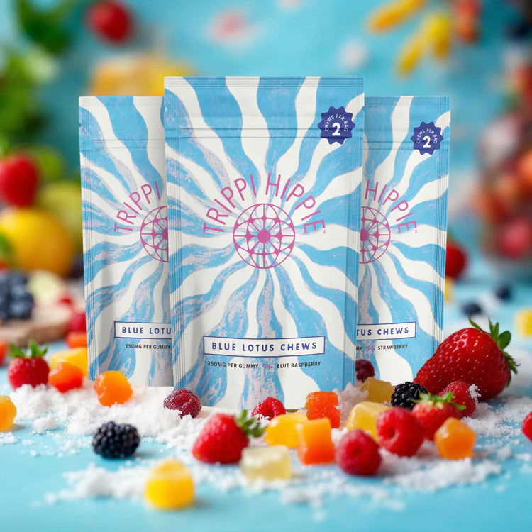Trippi Hippie Blue Lotus Chews- 3 bags with colorful packaging of white and blue swirls and "TRIPPI HIPPIE" on the front. The forefield, and background are gummy bears and berries on a blue background fruity background.