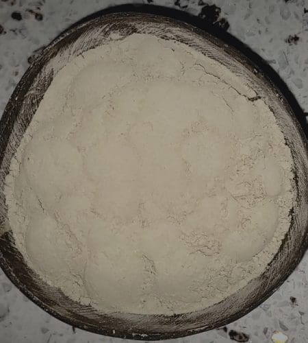 Round wooden bowl filled with a fine, light beige powder, set on a speckled surface.