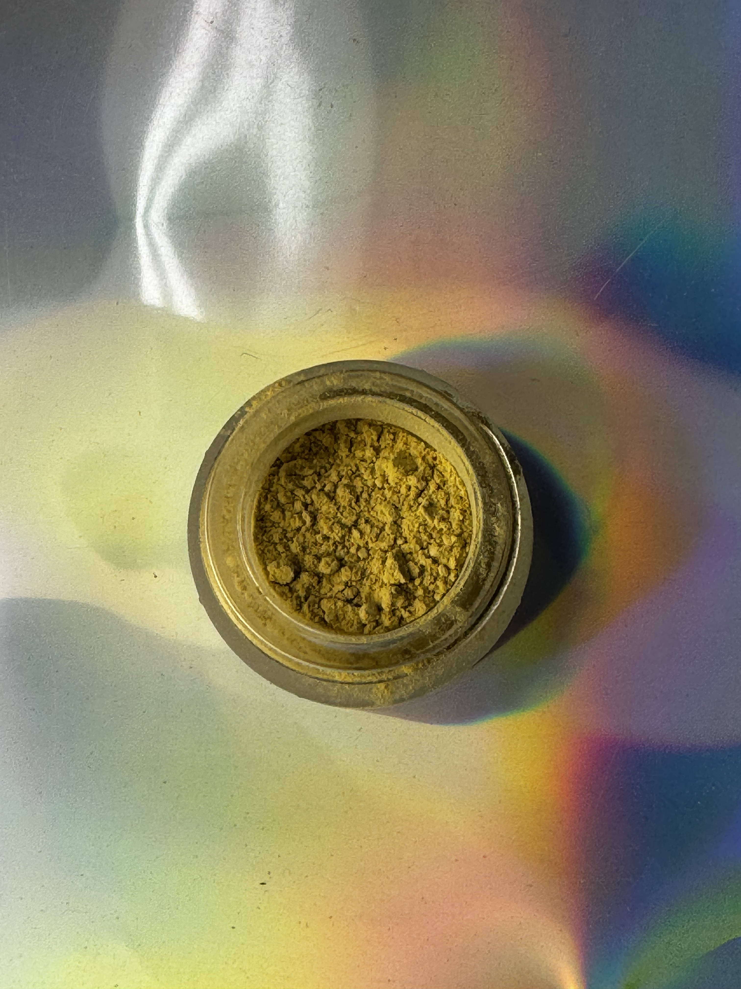 Jar of yellow kanna powder with a rainbow effect on a reflective rainbow surface
