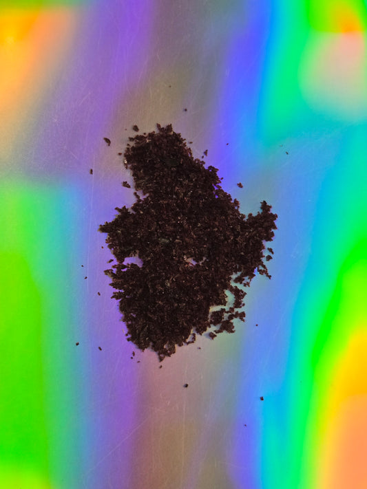 Top-down view of finely ground blue lotus (Nymphaea caerulea) extract displayed as a loose, dark botanical powder on a vibrant rainbow gradient background.