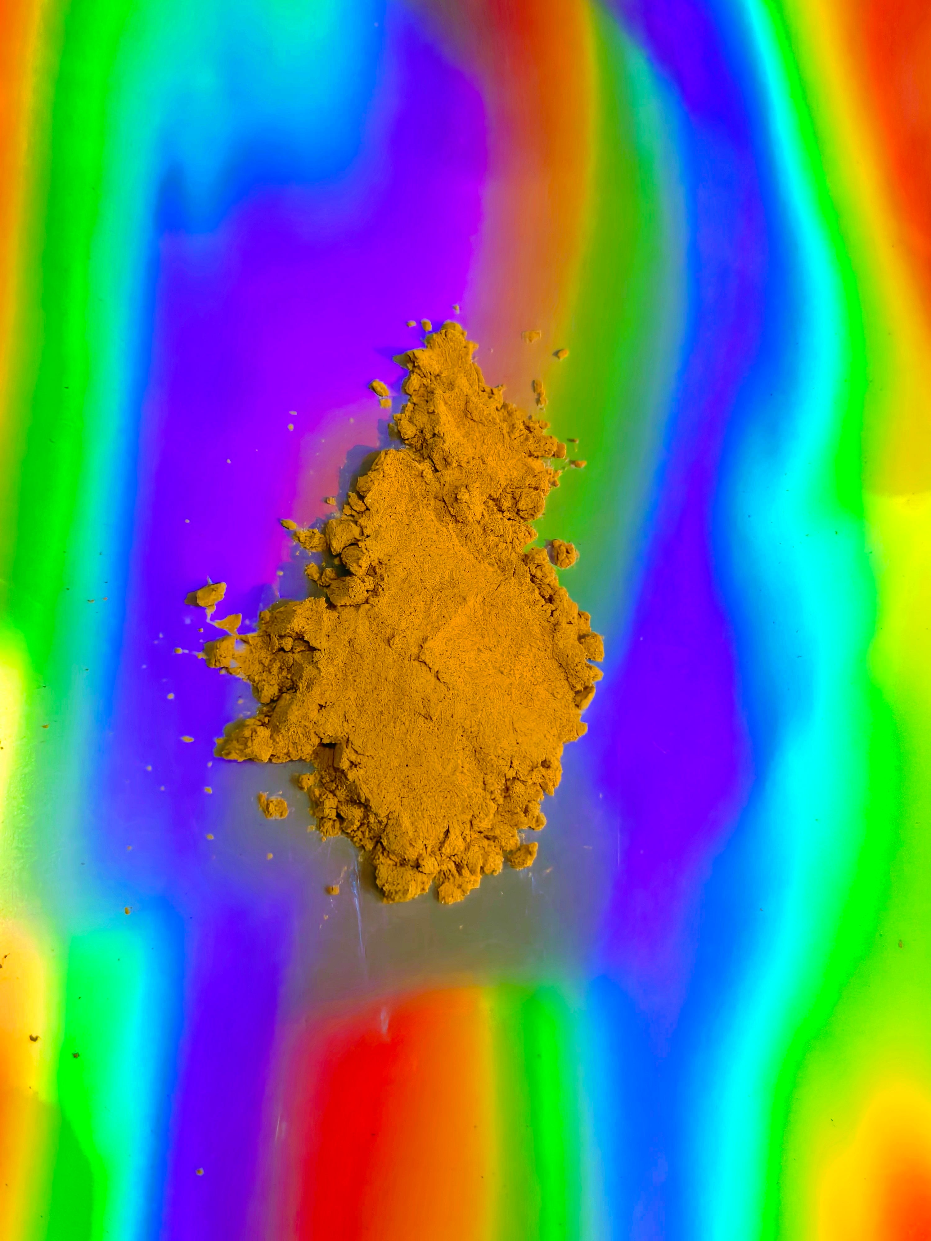 Fine golden-brown herbal extract powder arranged in a small mound on a vibrant iridescent rainbow background, highlighting smooth texture and purity.