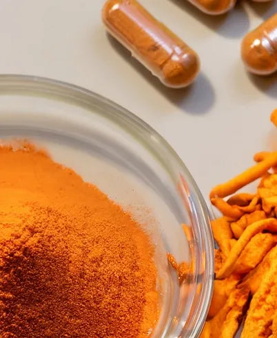 Close-up of cordyceps mushroom extract powder in a clear glass bowl, vibrant orange in color, with dried cordyceps pieces and filled capsules visible in the background.