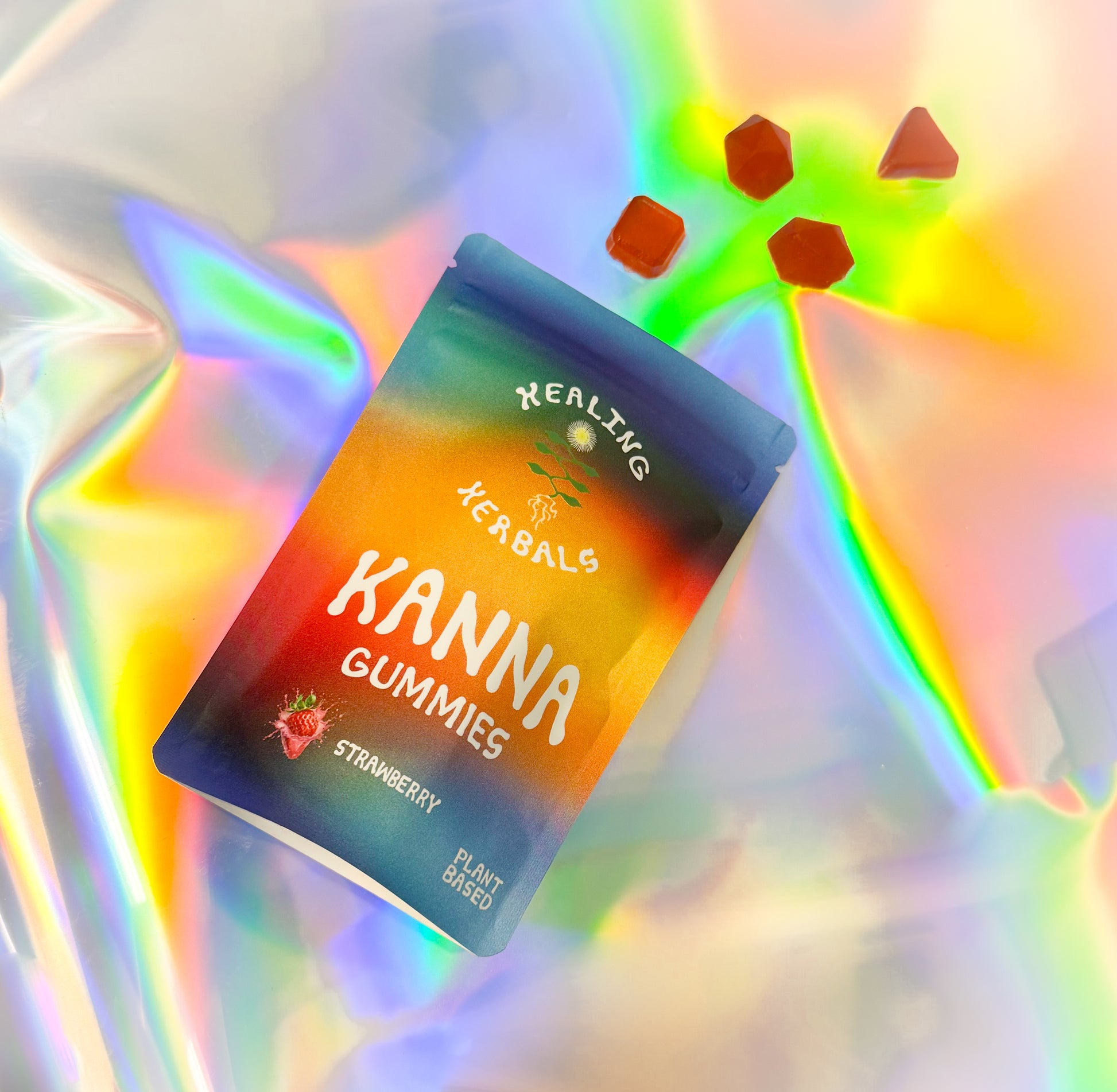 Healing Herbals strawberry kanna gummies in a colorful resealable pouch labeled “Kanna Gummies,” plant-based formula, displayed on an iridescent holographic background with several red gummy pieces scattered nearby.