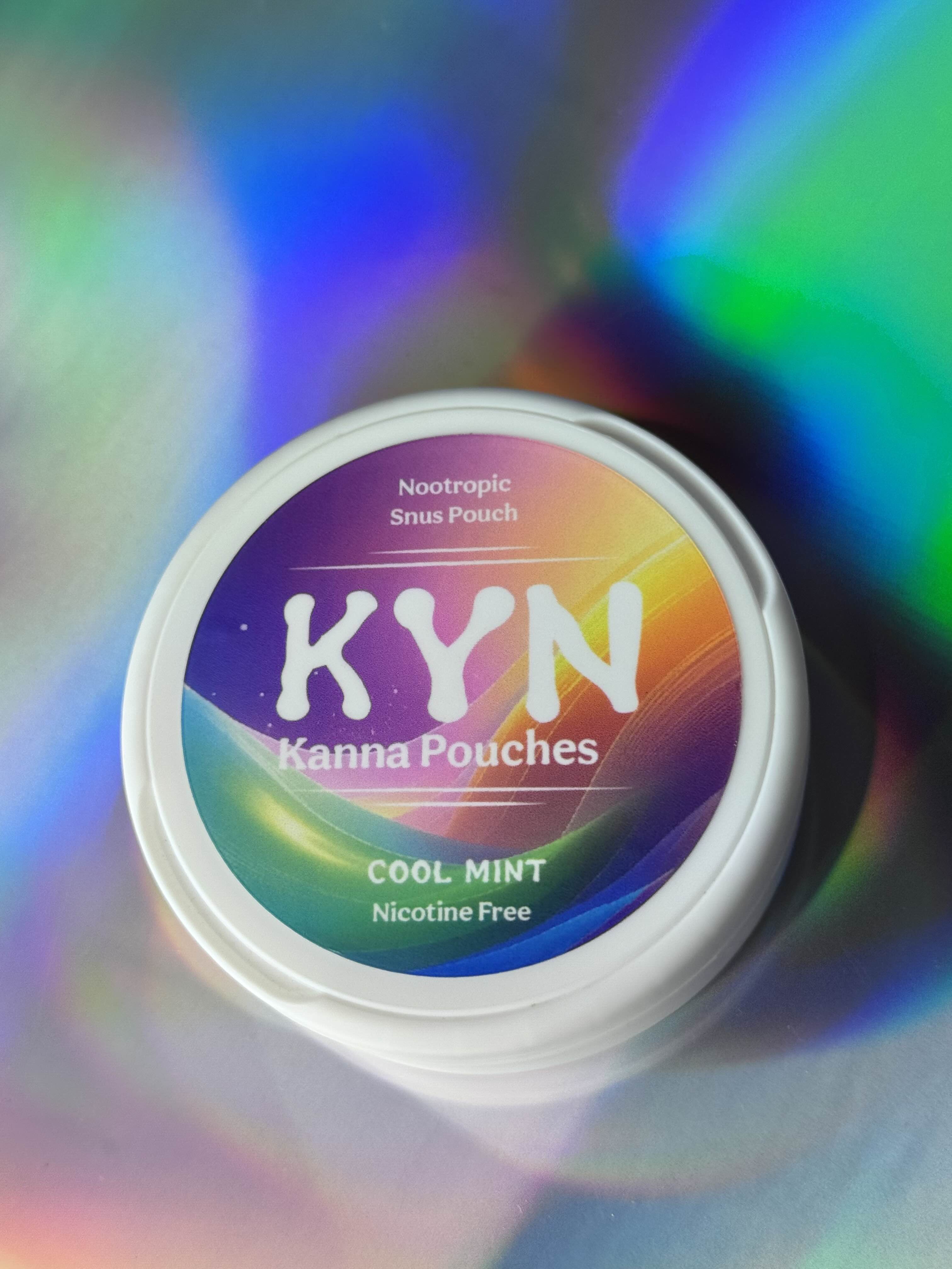 Top-down view of a round white container labeled “KYN Kanna Pouches – Cool Mint,” a nicotine-free nootropic snus pouch product, set against a colorful iridescent background.