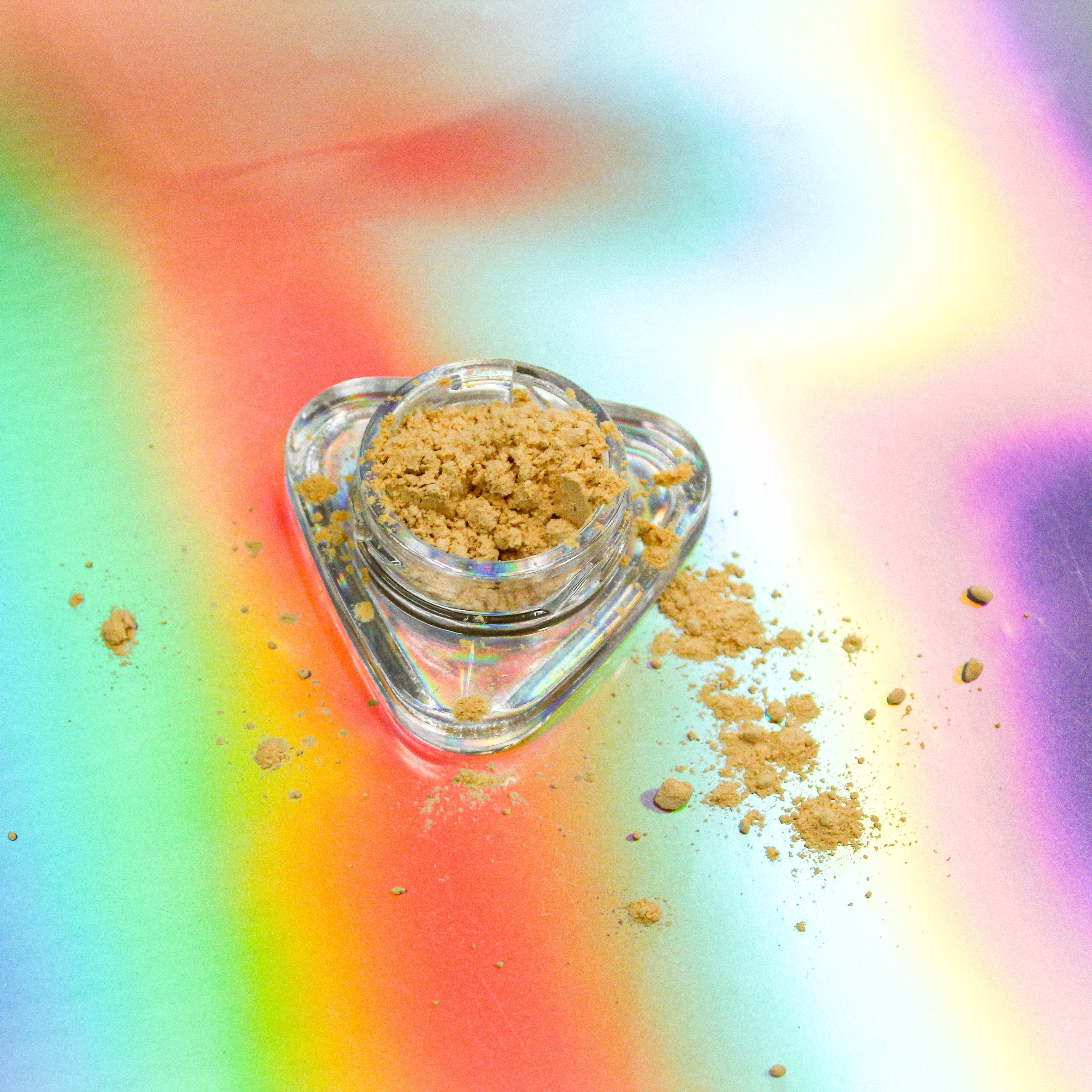 Full-spectrum kanna extract mix by Healing Herbals in a small clear glass jar, showing golden-beige powdered extract with scattered crumbs on a vibrant iridescent rainbow background.