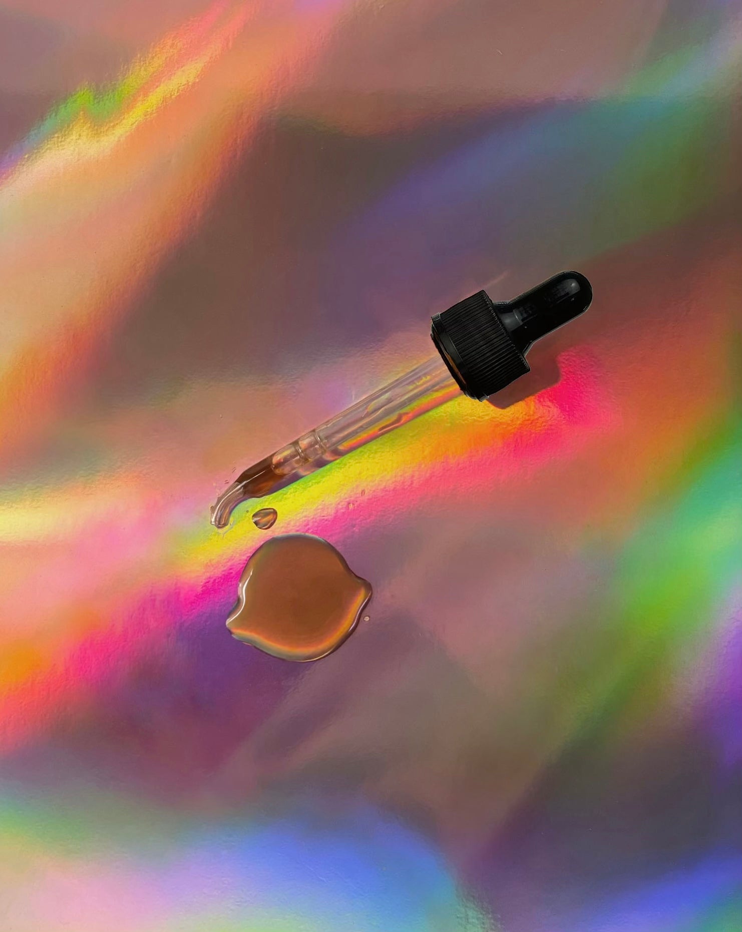 Glass dropper dispensing amber herbal tincture liquid onto a reflective iridescent surface, highlighting texture and clarity.