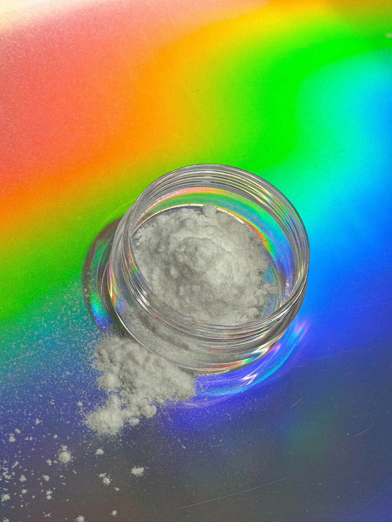 A small clear jar with a white powder filling 1/3rd of the jar over a colorful, gradient background. White powder is slightly spilled. 
