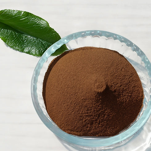 fine lobelia leaf extract powder in a clear glass bowl, rich brown in color, with a fresh green leaf placed alongside on a light surface.