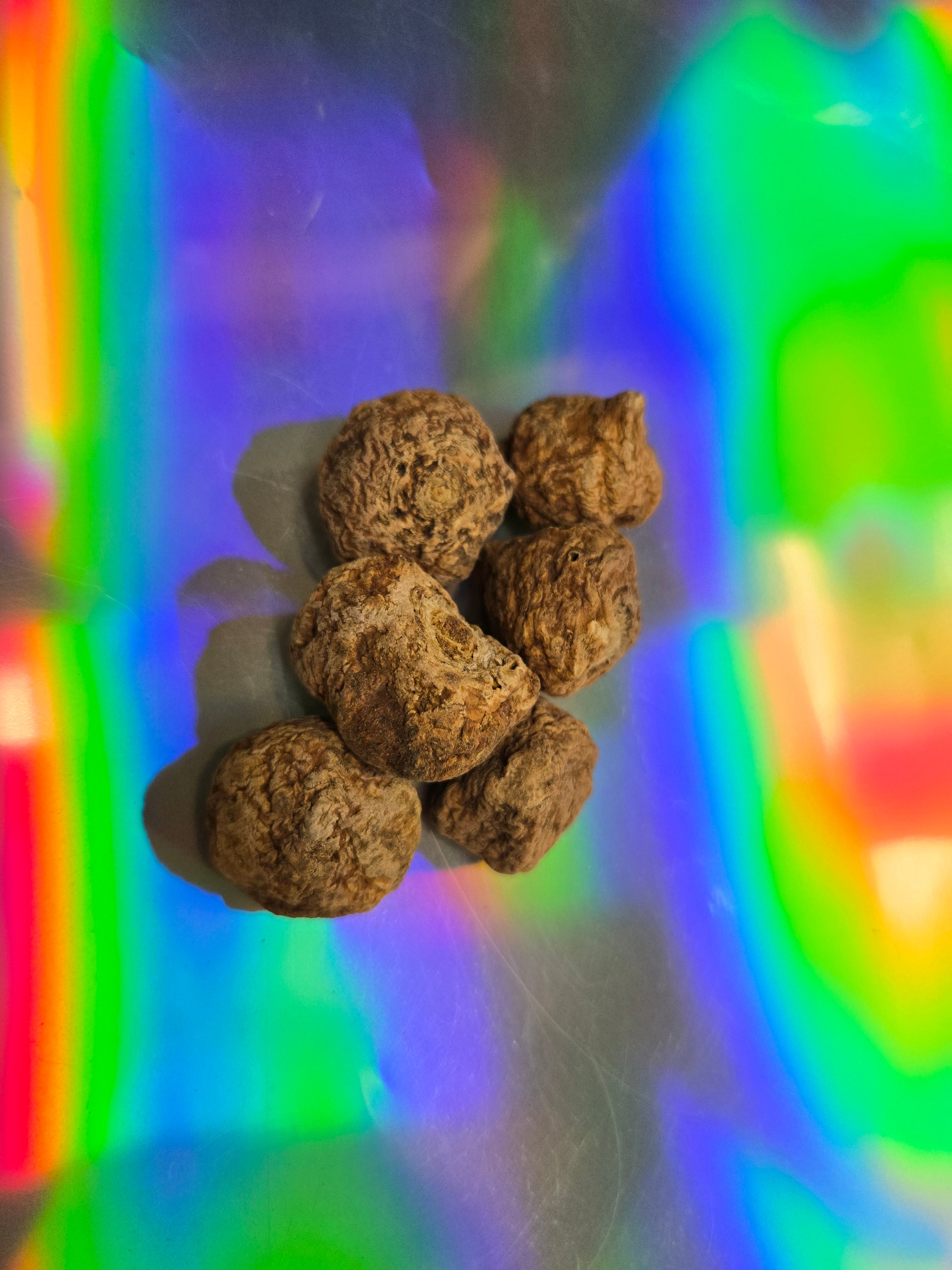 Top-down view of whole dried maca root bulbs with a rough, earthy brown texture, arranged on a vibrant holographic rainbow background.