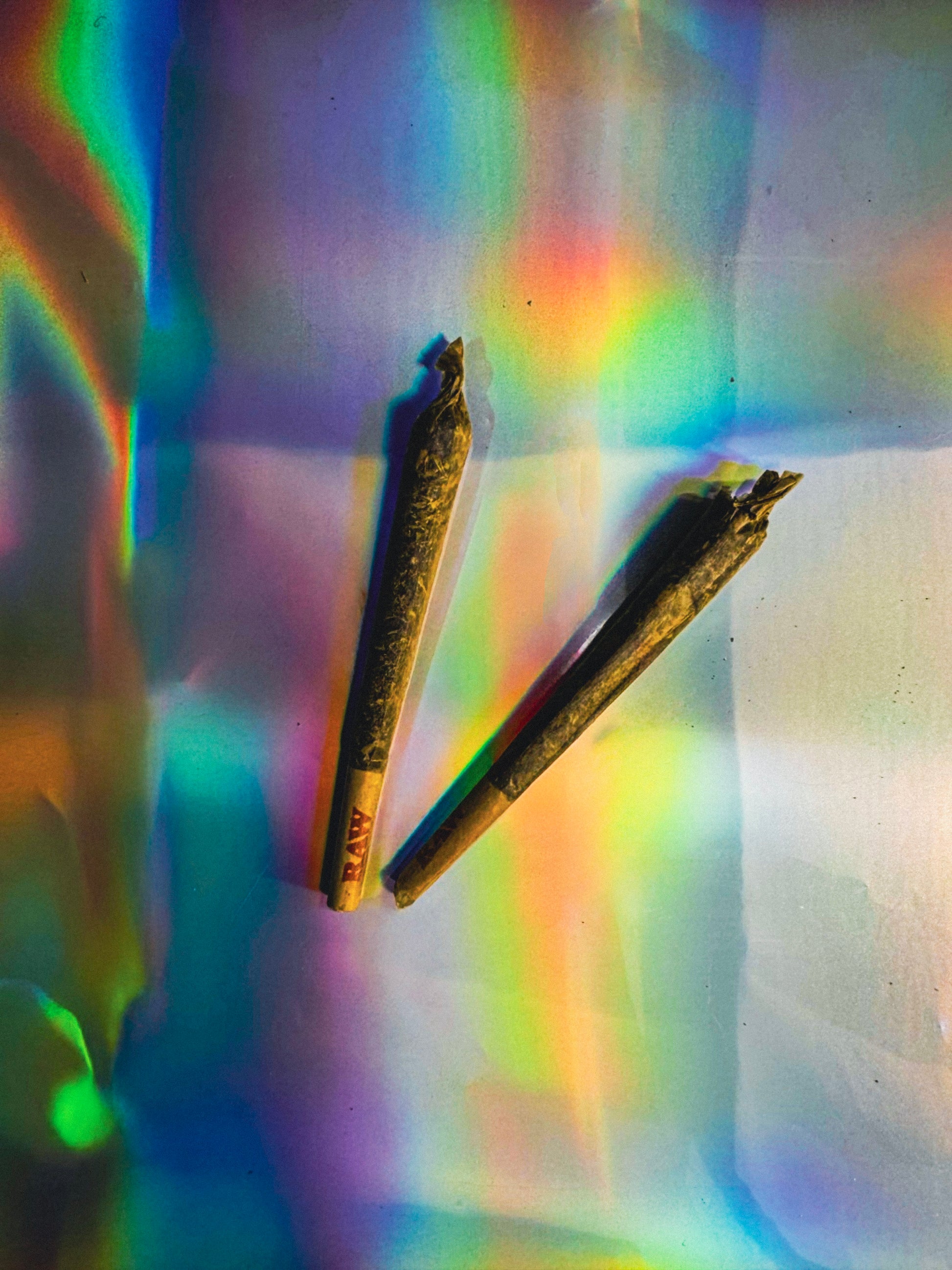 Two herbal joints on a colorful, iridescent surface