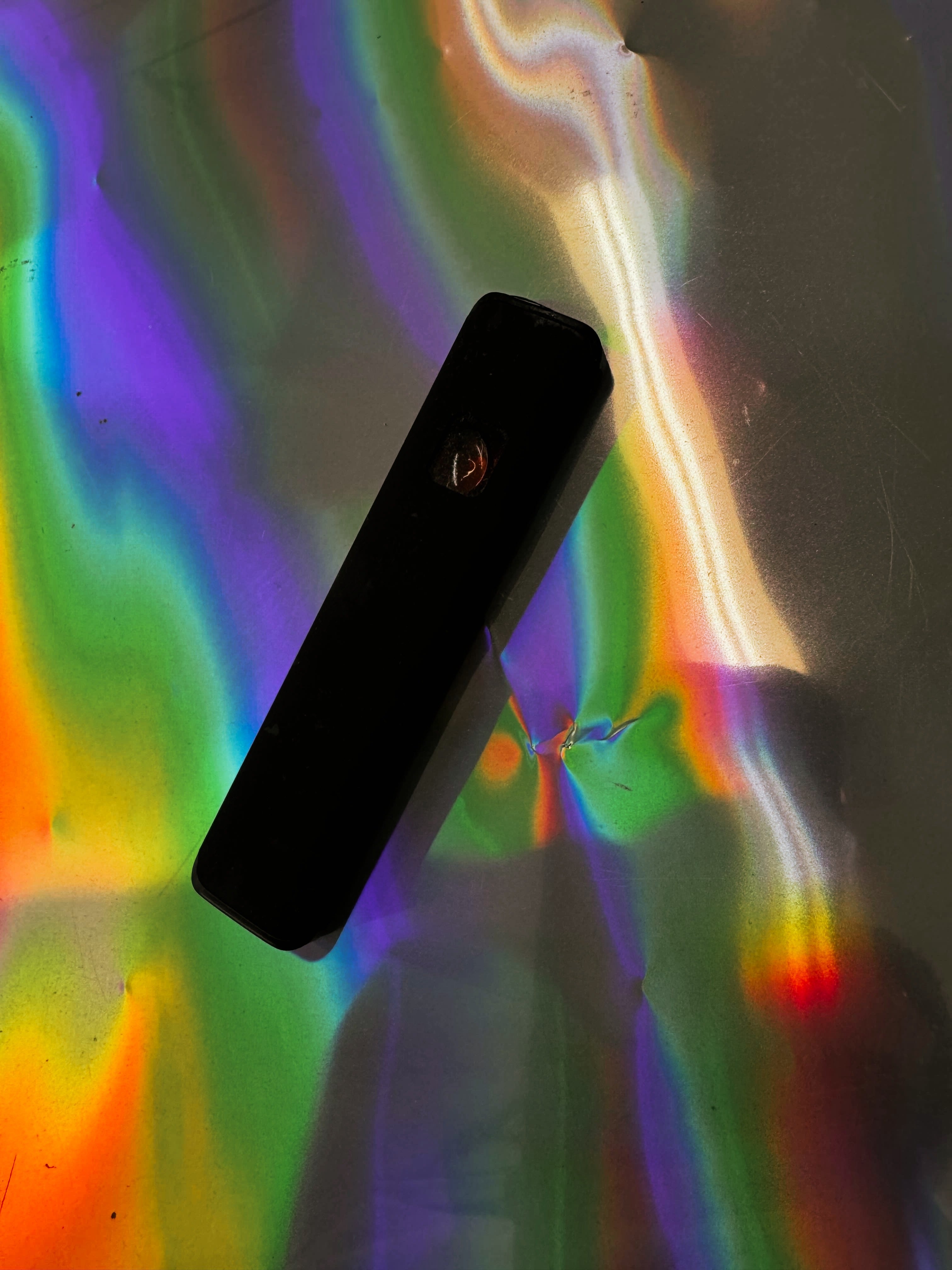 Minimalist black rectangular device with a smooth matte finish, displayed against a colorful, holographic rainbow backdrop.