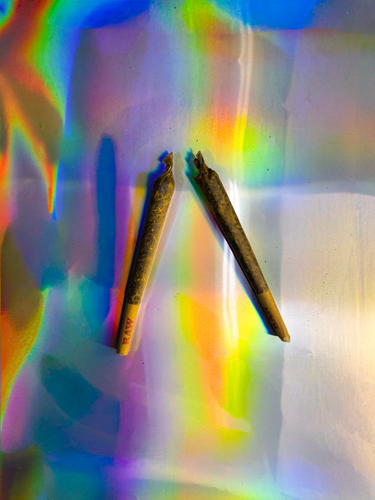 Pair of pre-rolled cones with RAW branded tips on iridescent rainbow surface, product display photo.